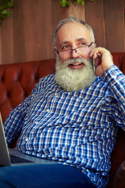 Mannen sitter i soffan och pratar i telefon — Stockfoto