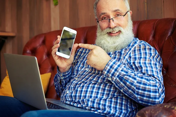 Äldre man pekade på smartphone och tittar på kameran — Stockfoto