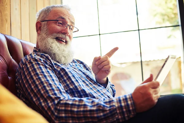 Äldre man sitter i soffan och pekar på TabletPC — Stockfoto