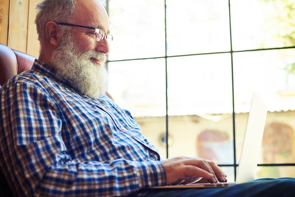 Alter Mann mit Brille sitzt auf dem Sofa und arbeitet mit Laptop — Stockfoto