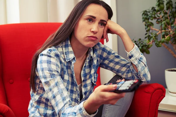 Sad woman sitting on the red chair and watching tv — Stock Photo, Image