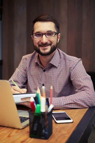 Um empresário satisfeito usando laptop no escritório e tomar notas — Fotografia de Stock
