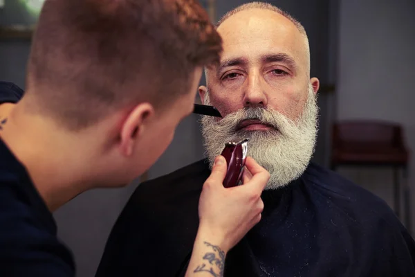 Парикмахер делает стрижку красивому привлекательному пожилому мужчине с беконом — стоковое фото
