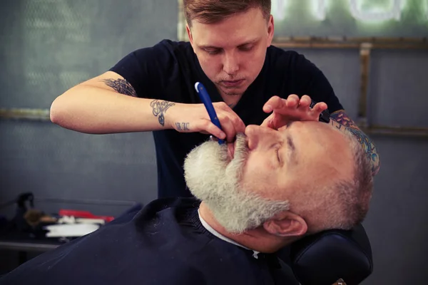 Schöner Friseur rasiert bärtigen Mann — Stockfoto