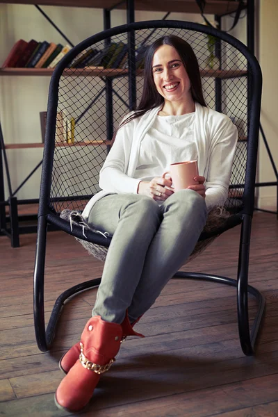 Laughing girl sitting in a chair with a cup — Stock Photo, Image