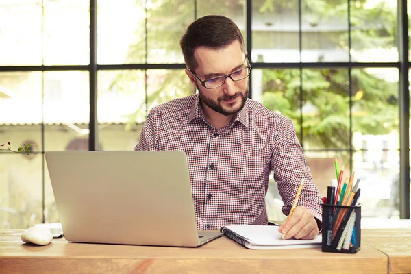 Mann benutzt Laptop und macht sich Notizen — Stockfoto