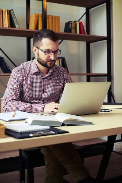 Mann mit Brille blickt auf seinen Laptop und tippt — Stockfoto