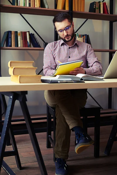 Человек в очках пишет заметки и использует ноутбук — стоковое фото