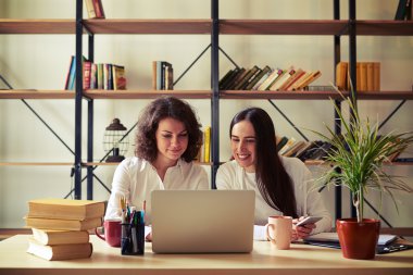 Bir dizüstü bilgisayar ve akıllı telefon çalışan iki genç kadın