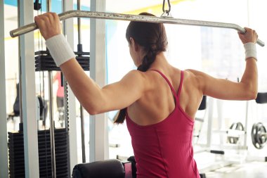 Woman is working out pull-down machine in gym