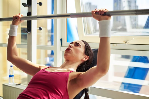 Femme presse un poids vers le haut dans la salle de gym près de la fenêtre — Photo