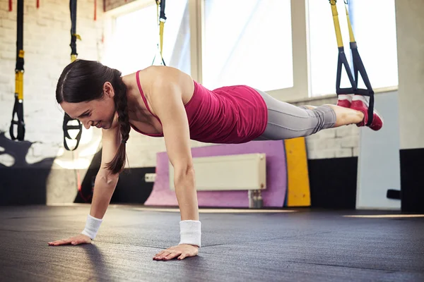 Joven morena está empujando en el trx — Foto de Stock