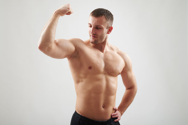 Young fit bare-chested man is showing biceps on his right arm isolated on white background