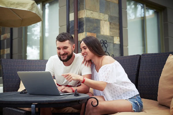 Usměvavý muž a žena na terase pozorují něco na laptopu — Stock fotografie