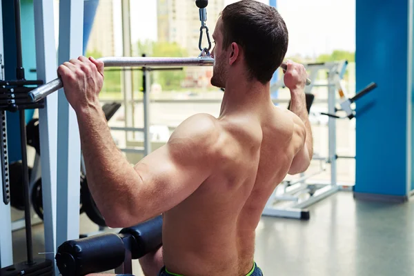 Člověk dělá ramena cvičení na stroji v tělocvičně — Stock fotografie