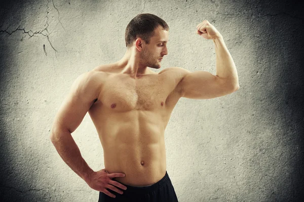 Człowiek pokazując biceps na lewym ramieniu nad betonowej ścianie — Zdjęcie stockowe