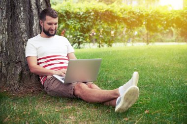 Young bearded man typing on laptop under the tree