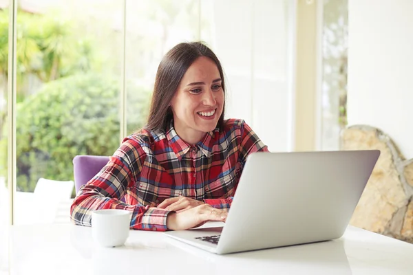 Donna attraente con tazza di caffè e laptop vicino alla finestra — Foto Stock