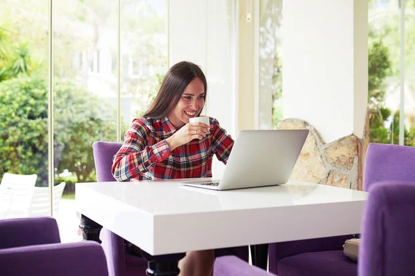 Young dark-haired woman enjoys coffee while working with laptop — Stok fotoğraf
