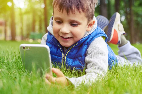 Petit garçon avec téléphone intelligent reposant sur l'herbe verte dans le parc — Photo