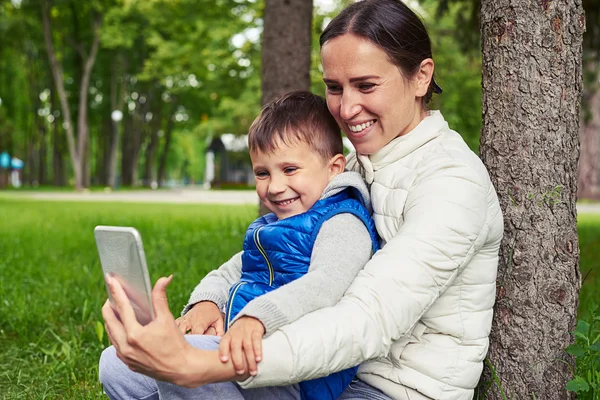 Moeder met kleine zoon kijken iets op slimme telefoon onder t — Stockfoto