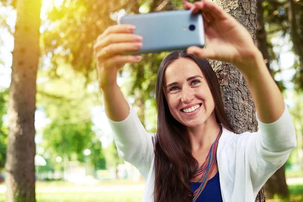 Sorridente signora fare un selfie sotto l'albero nel pittoresco parco — Foto Stock