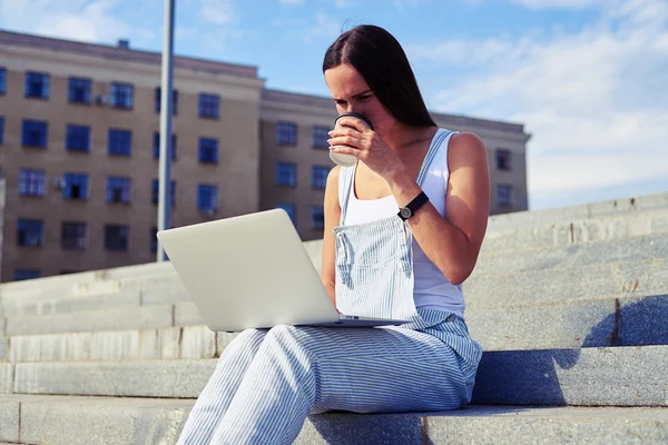 Bella donna che beve caffè e tiene il computer portatile in ginocchio — Foto Stock