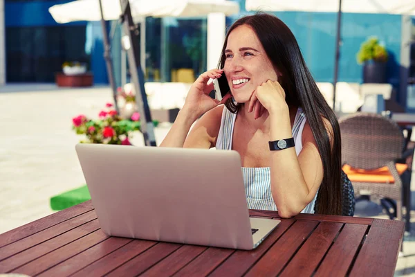 Hermosa mujer sonriente con portátil hablando por teléfono en caf —  Fotos de Stock