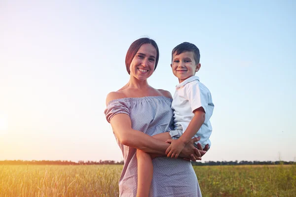 Schöne Frau und ihr kleiner Sohn auf dem Hintergrund des sonnenbeschienenen Feldes — Stockfoto