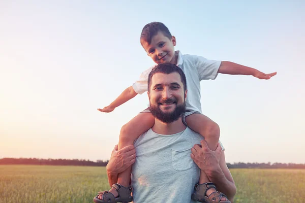 Padre caminando con su pequeño hijo sobre hombros en el campo — Foto de Stock