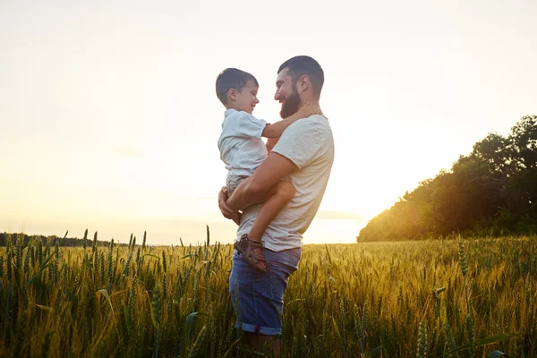 Vater hält kleinen Sohn bei schönem Sonnenuntergang im Feld — Stockfoto