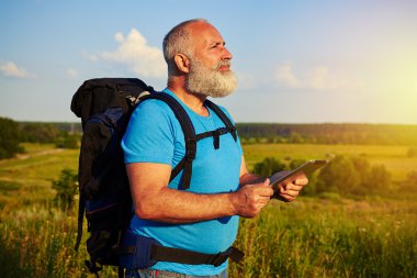 Bir veri tablet tutarak ve seyir içinde sırt çantası ile yaşlı erkek uygun