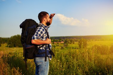 Otların arasında onun el kapsayan ayakta sırt çantası ile genç adam 
