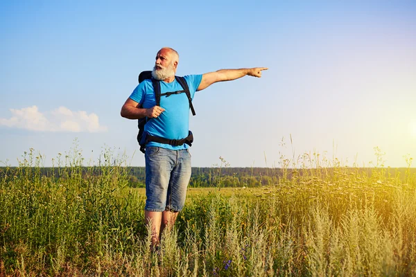 Hombre de edad activa con mochila apuntando a algo en el campo — Foto de Stock