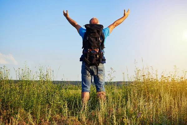 Vista posteriore di uomo anziano con zaino in piedi con le mani sollevate e — Foto Stock