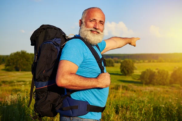 Fit aged man with rucksack is pointing at beautiful sunset in th — Stock Photo, Image
