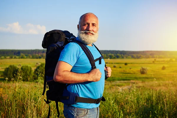 Fit aged tourist standing with rucksack against field background — Stock Photo, Image
