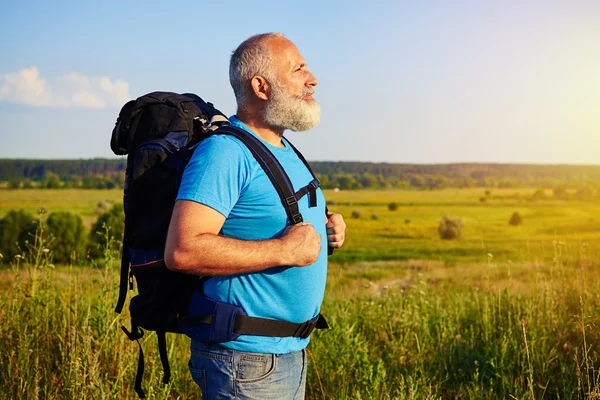 Widok z boku wieku człowieka noszenia plecaka przed pole backgrou — Zdjęcie stockowe
