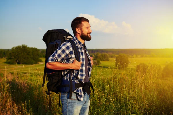 Vista lateral do homem com mochila em pé no campo e sorrindo — Fotografia de Stock