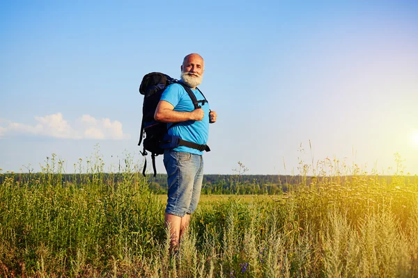 Portret mężczyzny w wieku z plecakiem stojący w polu na su — Zdjęcie stockowe