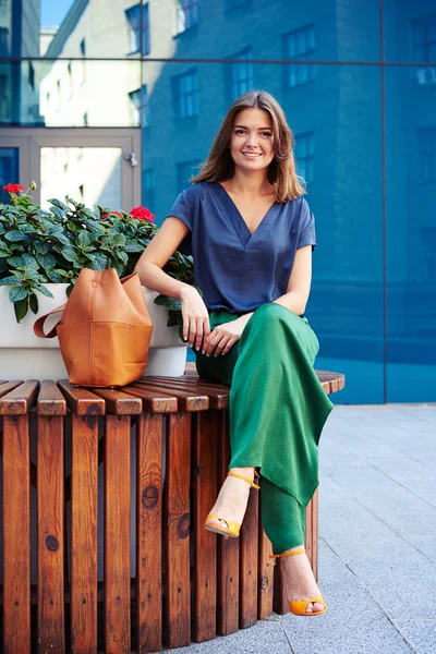 Mulher atraente sentado no banco redondo com vaso de flores e smil — Fotografia de Stock