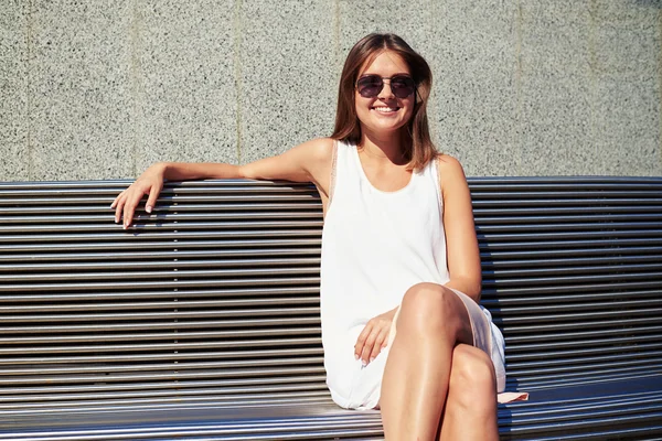 Young woman in sunglasses on bench near building wall smiling at — 스톡 사진