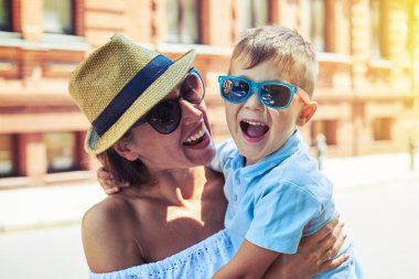 Küçük çocuk güneş gözlüğü wal sırasında annesinin kollarında gülüyor