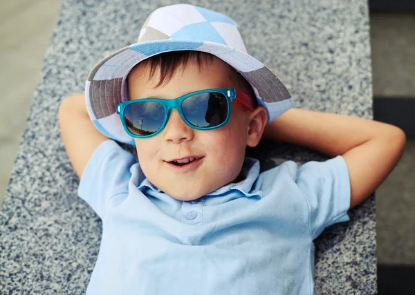 Радостный маленький мальчик в солнечных очках отдыхает на парапете уличной лестницы — стоковое фото