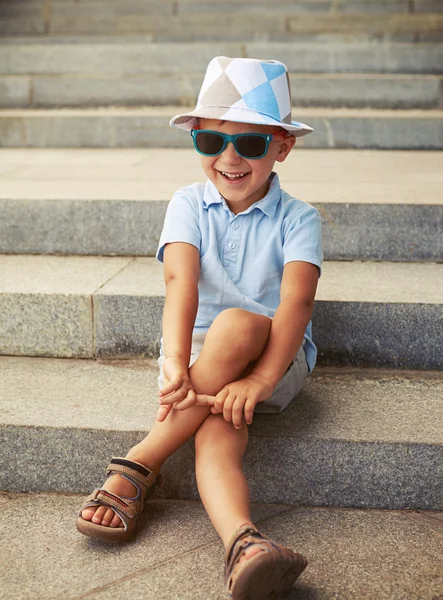 Πορτρέτο του μικρού αγοριού σε γυαλιά ηλίου και το καπέλο κάθεται και laughin — Φωτογραφία Αρχείου