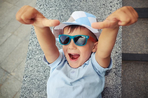 Joyful small boy in sunglasses giving two thumbs up while lying — Stock Photo, Image