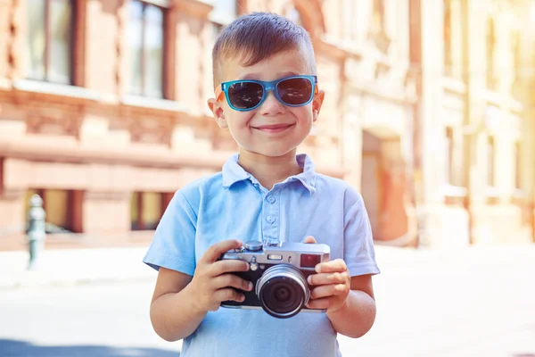 Küçük çocuk güneş gözlüğü ile fotoğraf makinesi arka plan üzerine poz — Stok fotoğraf