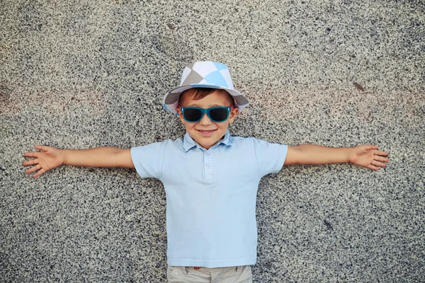 Маленький хлопчик стоїть біля стіни на вулиці з розкиданими руками — стокове фото