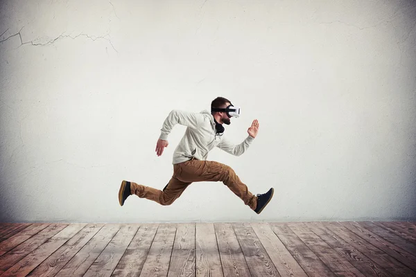 Young man in virtual reality headset in jump over wooden floor — Stock Photo, Image