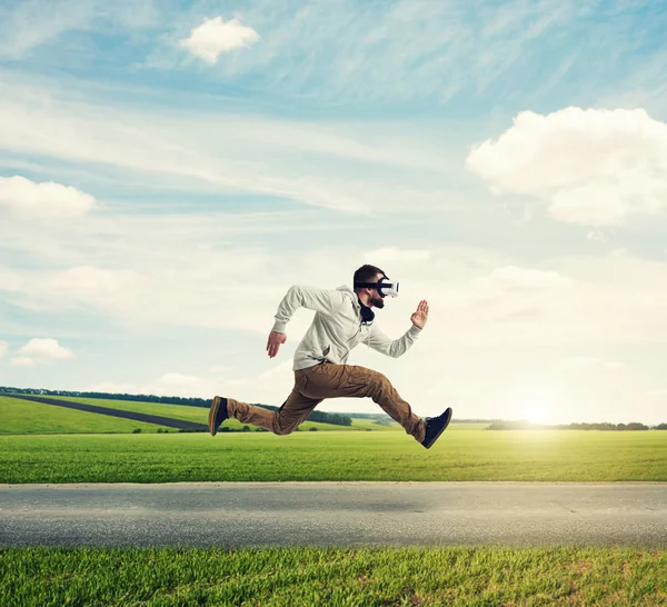 Hombre joven con auriculares de realidad virtual corriendo a lo largo del prado —  Fotos de Stock